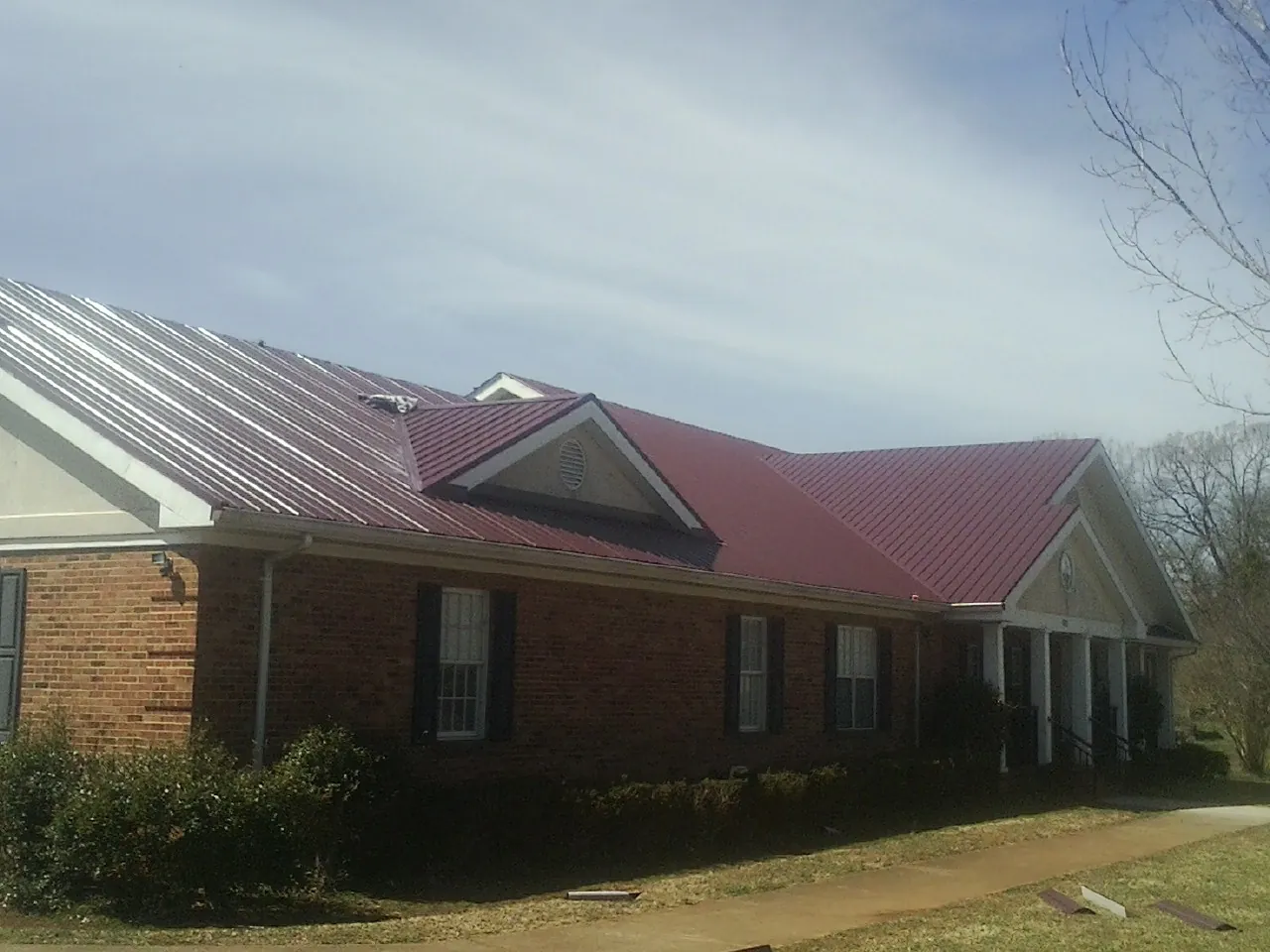 Red metal roof with gabled entries on a long brick building, from a Hail Damage Roof Repair job in Dupont
