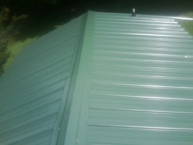 New green metal panels meeting at the ridge of a roof — Flat Roof Repair work by our crew in Dupont