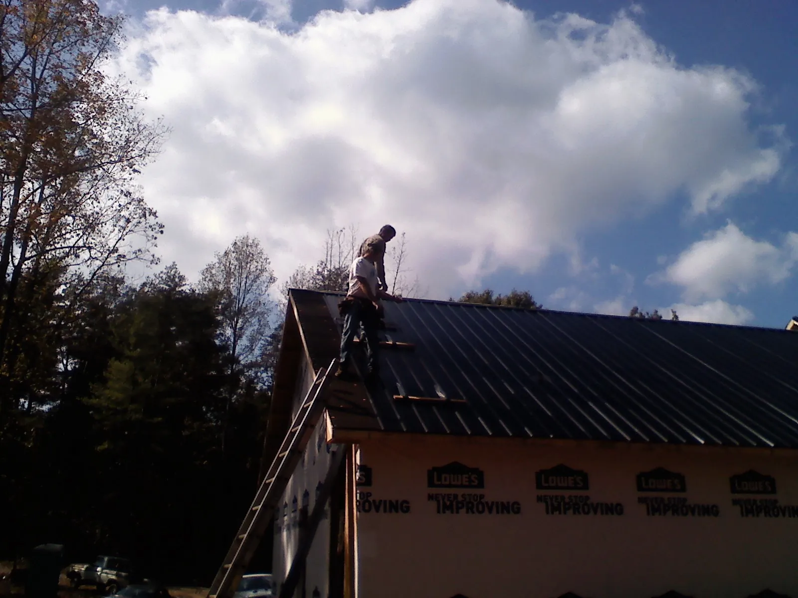 Roofer fastening dark metal panels high against a cloudy sky, from a Roof Inspection job in Dupont