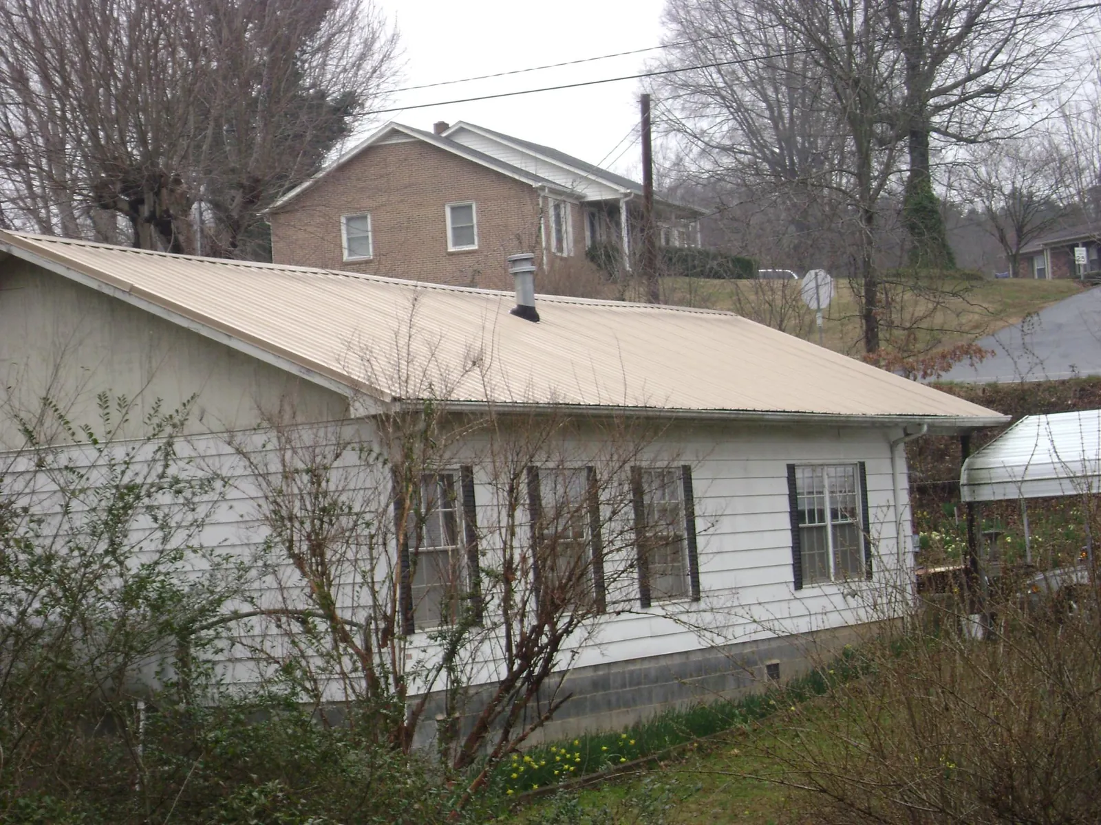 Tan metal roof on a white sided house set into a hillside — Commercial Roofing by Roofing Brothers in Dupont